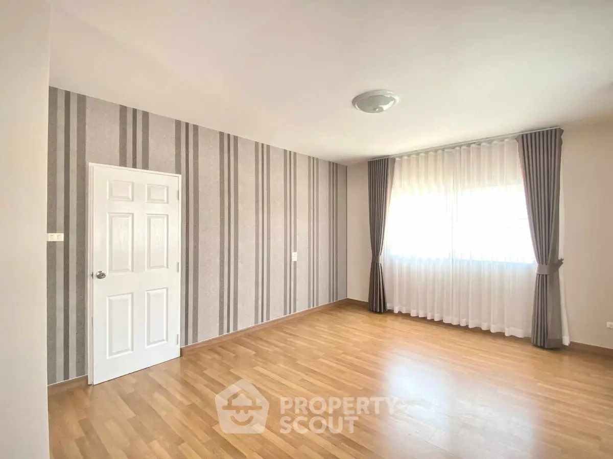 Spacious empty room with striped wallpaper and wooden flooring, ideal for customization.
