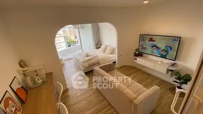 Modern living room with cozy seating and large TV, featuring a bright bedroom view.