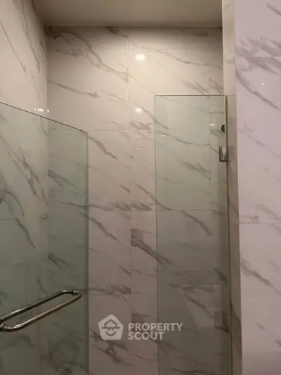 Luxurious marble-tiled bathroom with sleek glass shower enclosure.