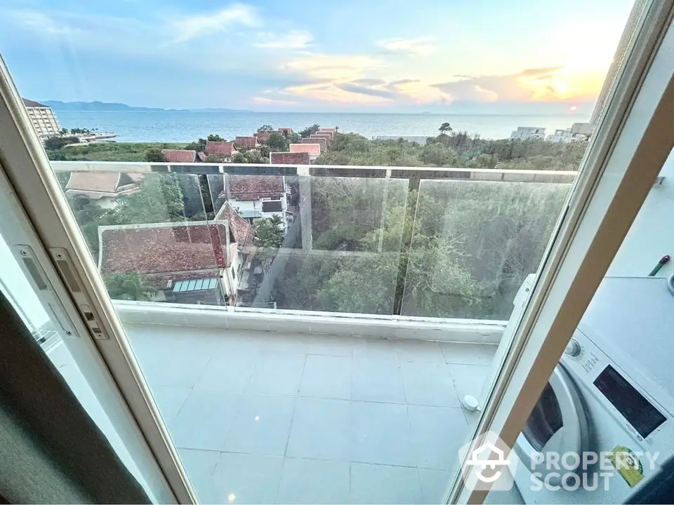 Stunning balcony view with ocean and sunset, featuring modern glass railing and washing machine.