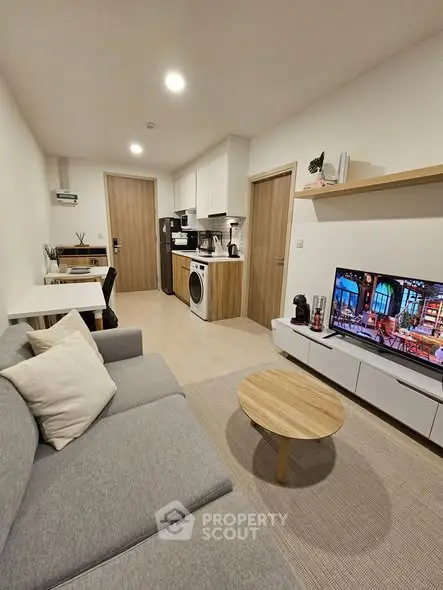 Modern living room with cozy gray sofa, TV, and compact kitchen area.