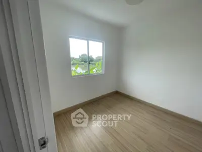Bright empty room with wooden flooring and large window offering serene nature view.