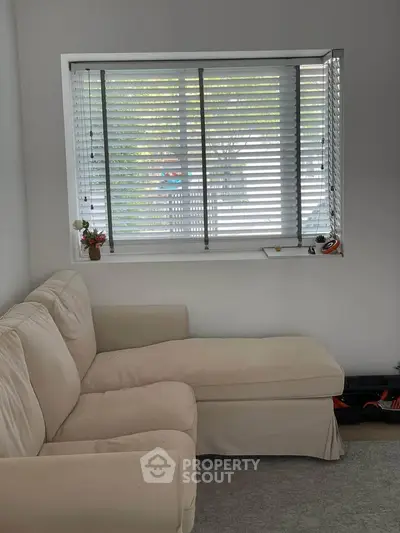 Cozy living room with beige sectional sofa and window blinds, perfect for relaxation.