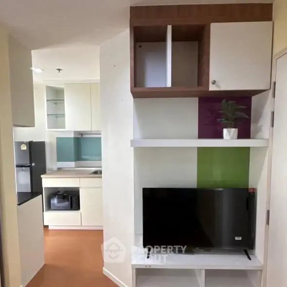 Modern apartment interior with compact kitchen and living area featuring a flat-screen TV and stylish shelving.