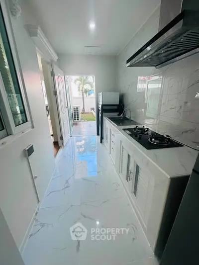 Sleek modern kitchen with marble flooring and gas stove, leading to a bright outdoor view.