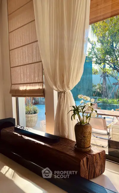 Elegant living room with large window, sheer curtains, and garden view, featuring a stylish wooden bench and potted plant.