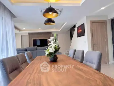 Elegant dining area with modern lighting and wooden table in a stylish open-plan living space.