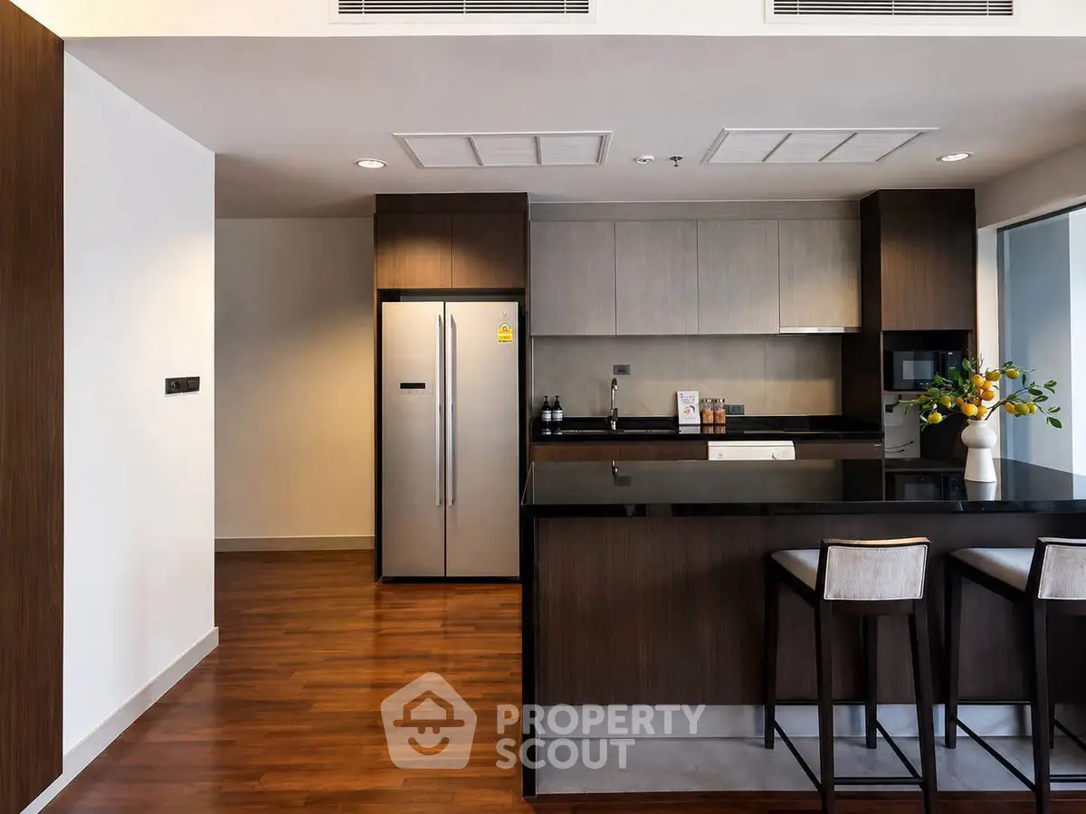 Modern kitchen with sleek design, featuring a large fridge and stylish bar seating.