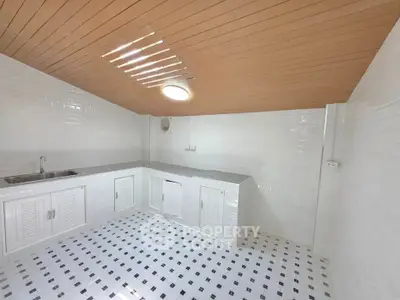 Spacious white-tiled kitchen with wooden ceiling and ample storage space.