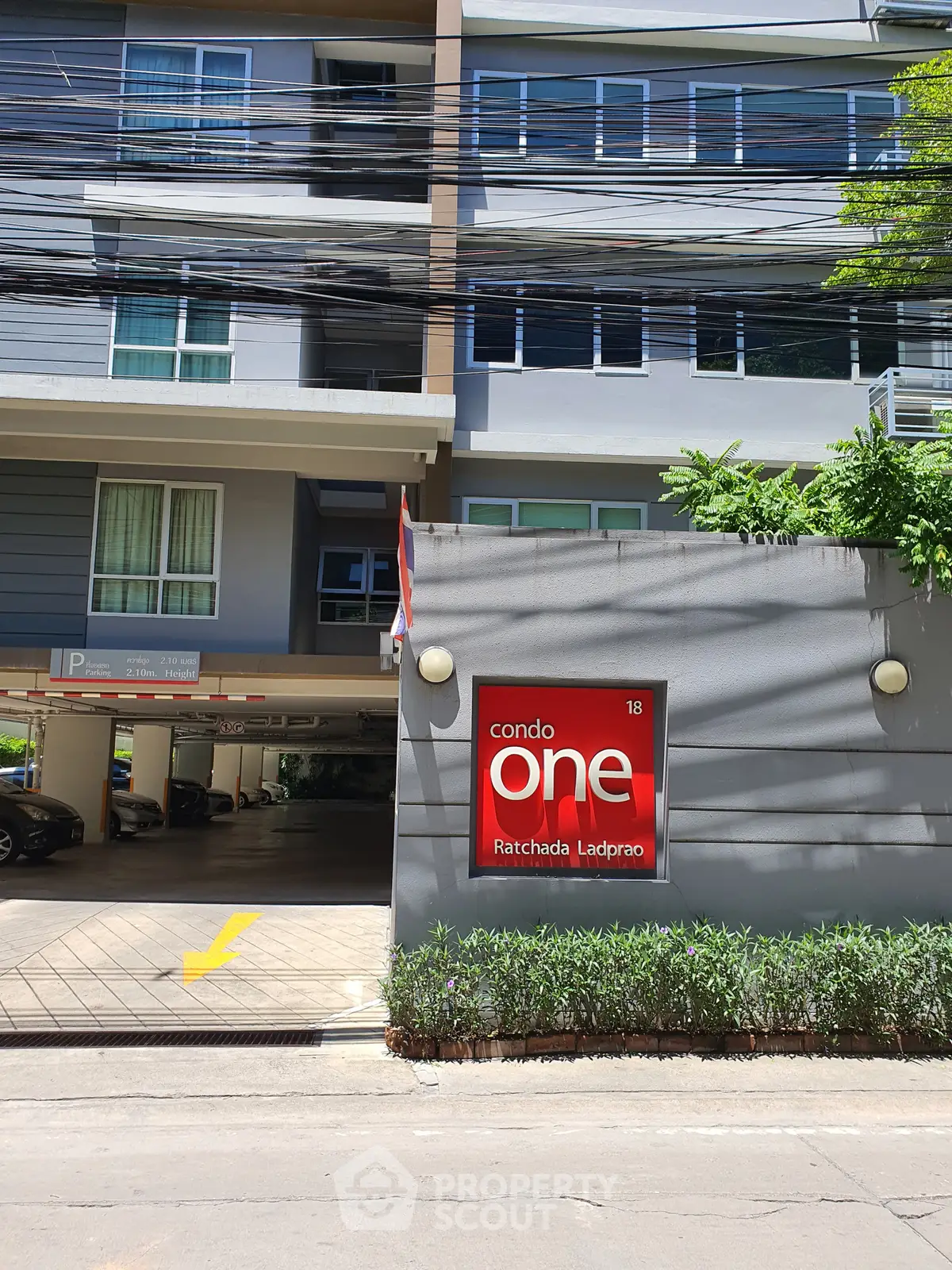 Modern condo building exterior with parking area and lush greenery, ideal urban living.