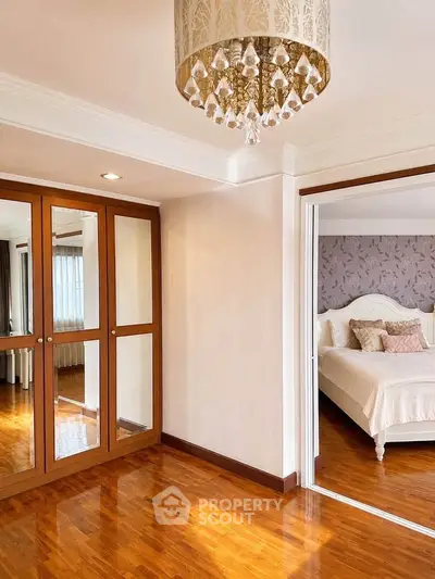 Elegant bedroom with wooden flooring and chandelier, featuring a mirrored wardrobe and a glimpse of a cozy bed.
