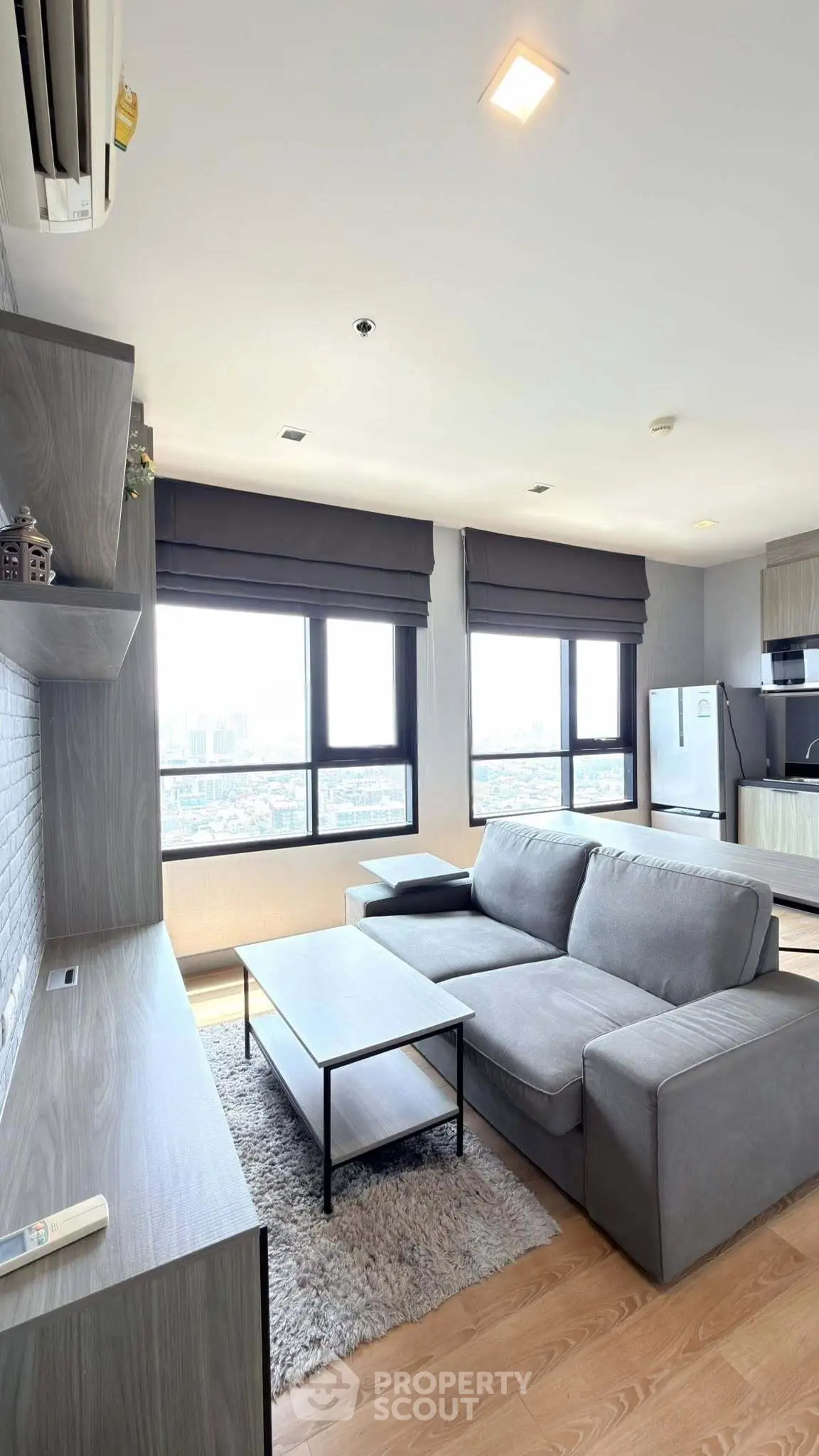 Modern living room with large windows and city view, featuring a cozy gray sofa and sleek wooden furniture.