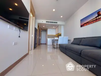 Modern apartment interior with sleek finishes, featuring a spacious living area, glossy tiled flooring, and a cozy dark sofa set against a white wall with vibrant artwork.