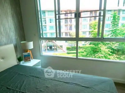 Bright bedroom with large window offering a view of lush greenery and modern apartment building.
