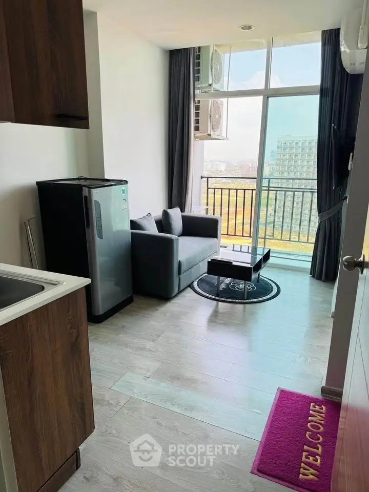Modern living room with balcony view, compact sofa, and sleek kitchenette in a high-rise apartment.