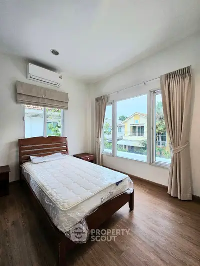 Cozy bedroom with large windows and wooden flooring, offering a serene view of the neighborhood.