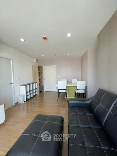 Spacious modern living room with sleek black leather sofas and elegant dining area.