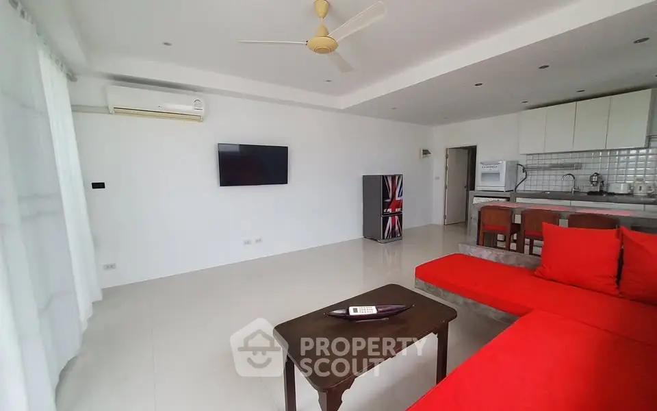 Spacious living room with modern red sofa and open kitchen layout, perfect for entertaining.