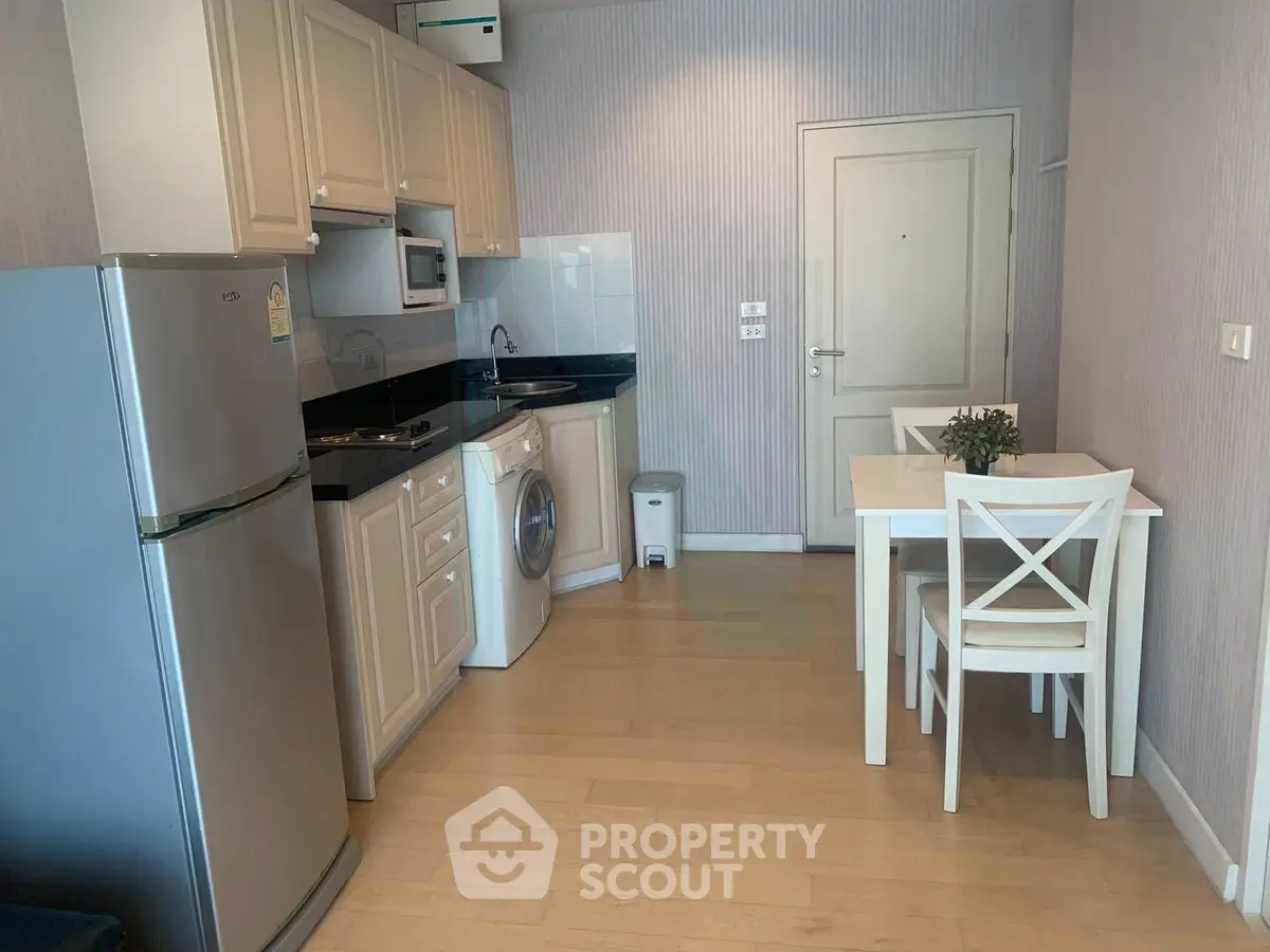 Modern kitchen with dining area, featuring appliances like fridge and washing machine, in a cozy apartment setting.
