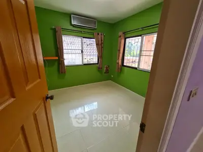 Bright and airy bedroom with vibrant green walls, large windows with burgundy curtains, and glossy white floor tiles, offering a refreshing living space.