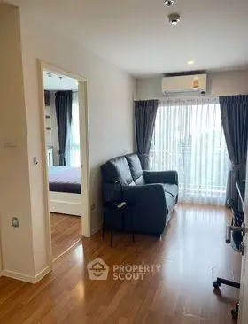 Modern living room with wooden flooring and natural light, featuring a cozy sofa and air conditioning.