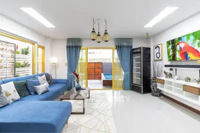 Spacious living room with modern decor and vibrant colors, featuring a large blue sofa and wall-mounted TV.