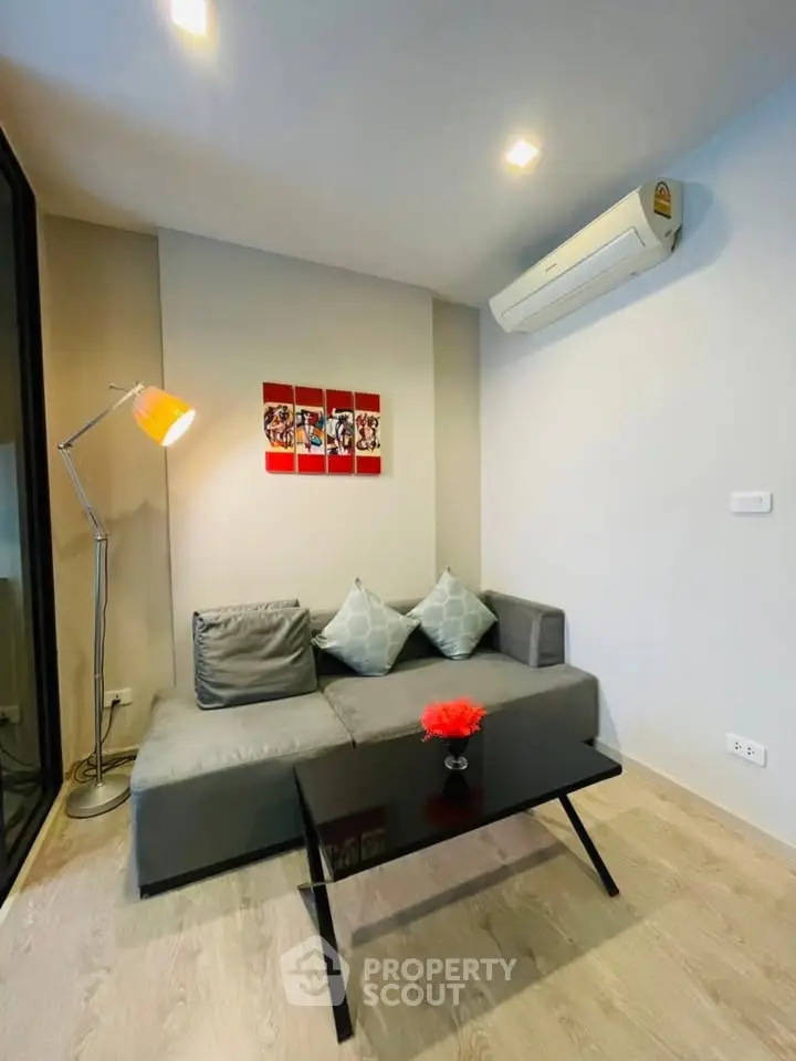 Modern living room with stylish decor and air conditioning, featuring a cozy gray sofa and vibrant artwork.