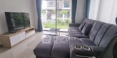 Modern living room with plush gray sofa and large TV, overlooking a garden view.