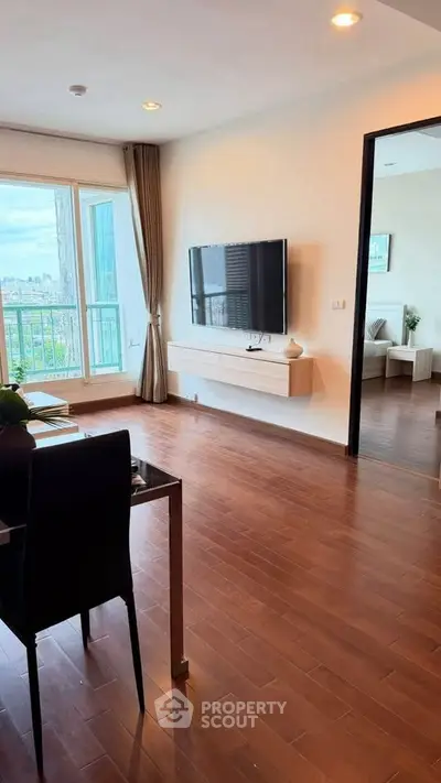 Modern living room with wooden flooring and city view, featuring a wall-mounted TV and elegant decor.