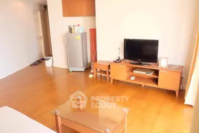 Spacious living room with wooden flooring and modern furniture, featuring a TV and glass coffee table.