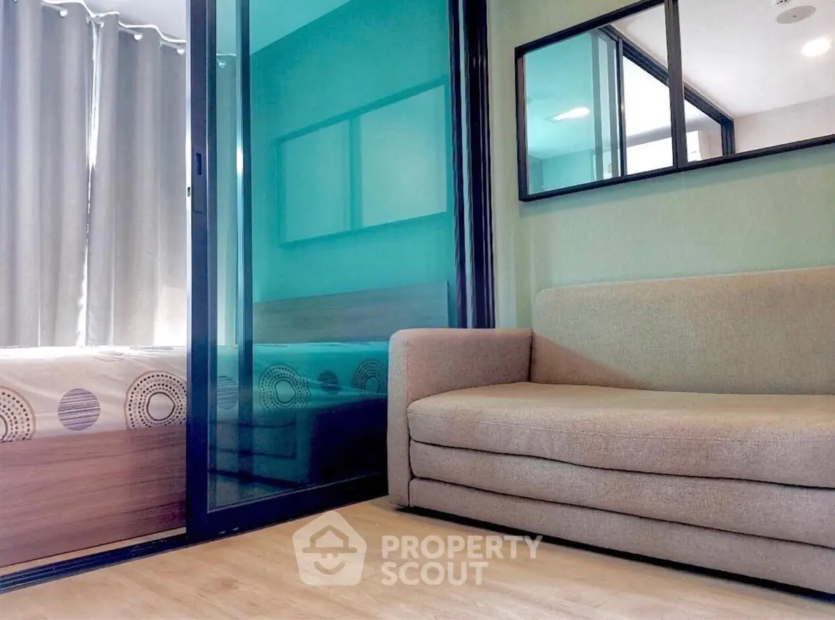 Modern living room with cozy sofa and glass partition leading to bedroom.