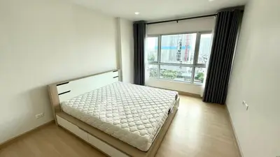 Spacious bedroom with large window offering city views, featuring a modern bed and light wood flooring.