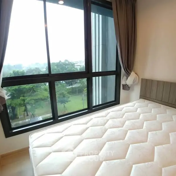 Bright bedroom with large windows offering a serene garden view, featuring a comfortable mattress and elegant curtains.