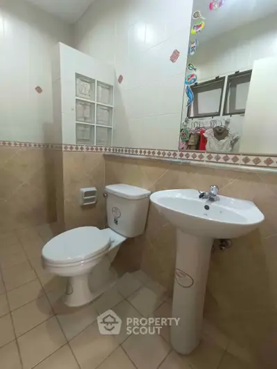 Spacious bathroom with modern fixtures and tiled walls, featuring a pedestal sink and toilet.