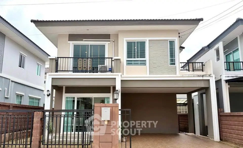 Modern two-story house with balcony and gated driveway in suburban neighborhood.