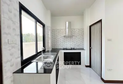 Modern kitchen with sleek black countertops and gas stove, featuring large windows for natural light.
