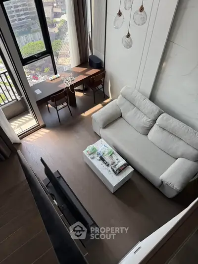 Modern living room with high ceiling and large windows offering city views, featuring a cozy sofa and stylish decor.