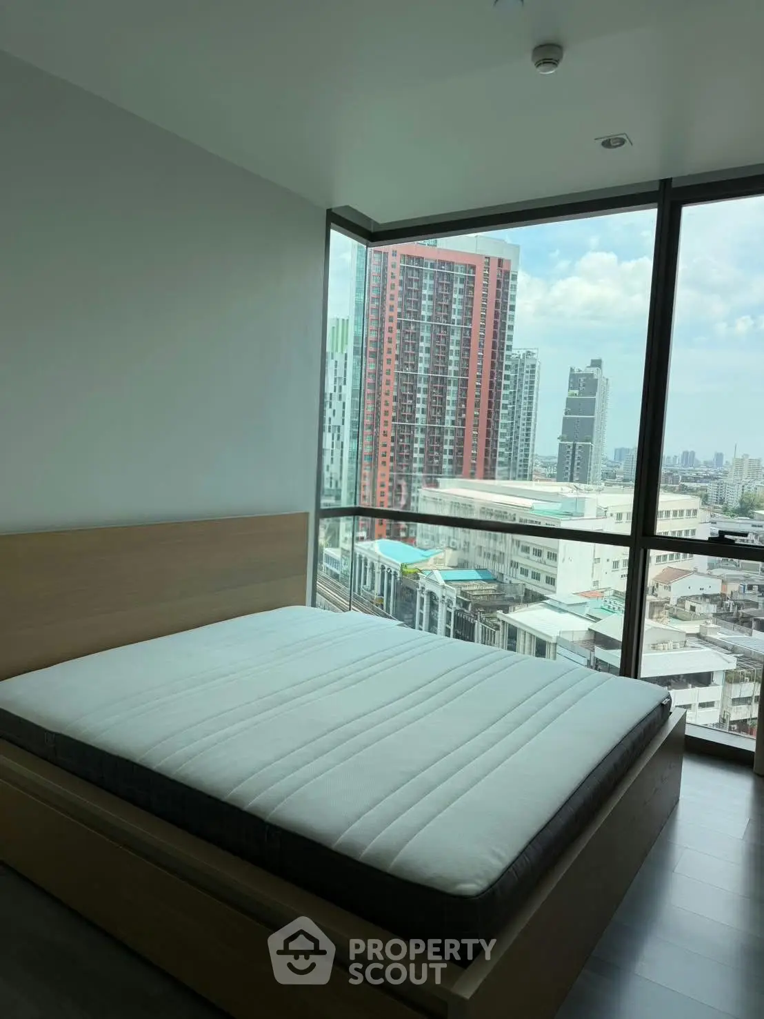 Modern bedroom with large windows offering stunning city views in a high-rise apartment.