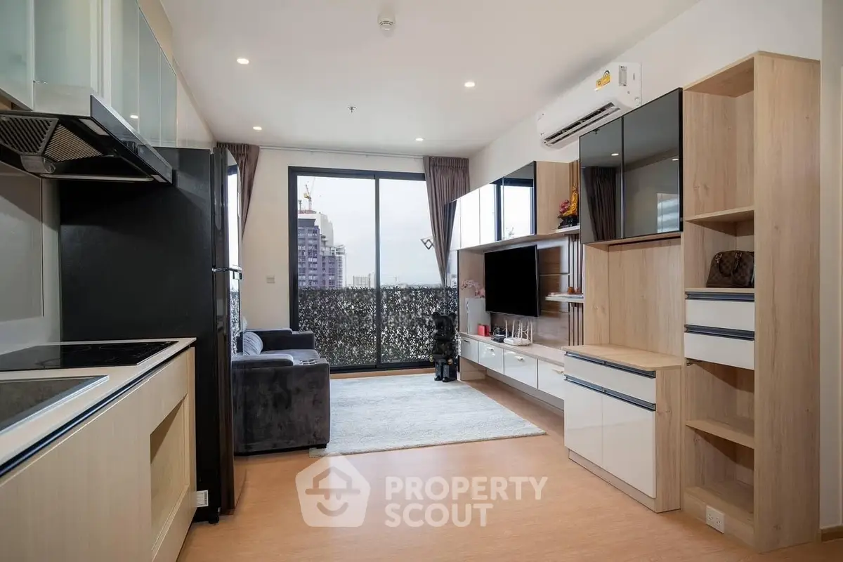 Modern living room with open kitchen, featuring sleek cabinetry and large windows with city view.