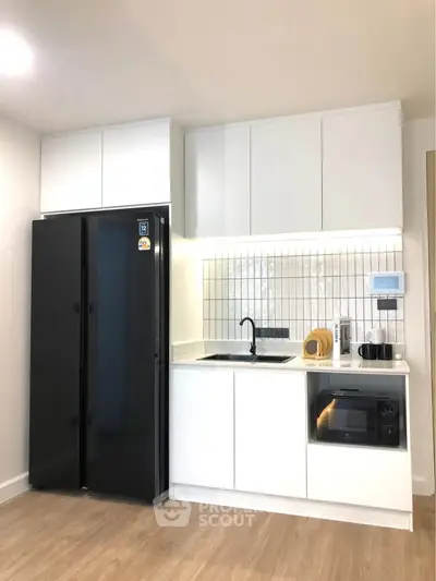 Modern kitchen with sleek black fridge and built-in oven in stylish apartment.
