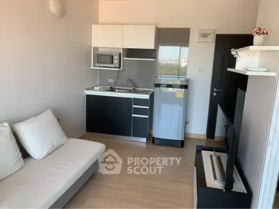 Modern compact living room with kitchenette, featuring sleek black and white cabinetry and cozy seating.