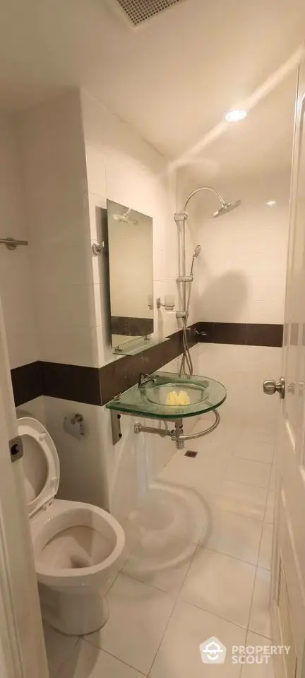 Modern bathroom with glass sink and rainfall shower in sleek white tiles.