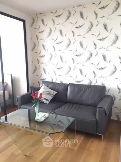 Stylish living room with modern sofa and glass coffee table, featuring elegant feather-patterned wallpaper.