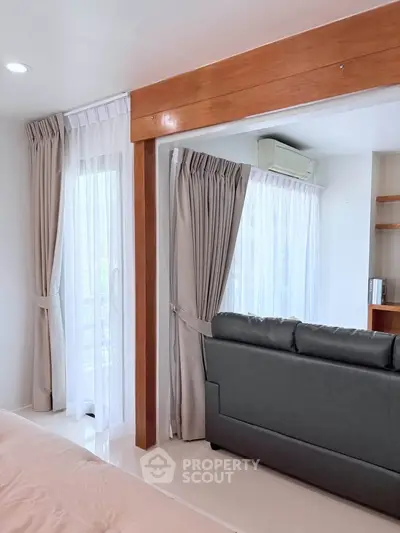 Spacious living room with elegant curtains and modern sofa, featuring natural light and stylish wooden accents.