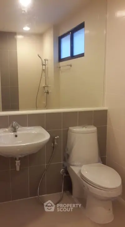 Modern bathroom with sleek fixtures and neutral tiles, featuring a shower and toilet.