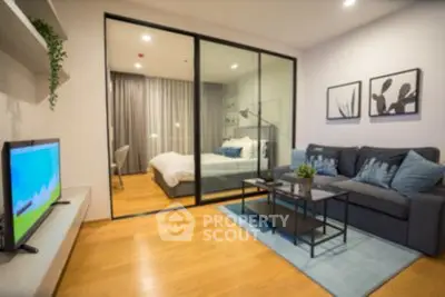 Modern living room with glass partition to bedroom, featuring sleek furniture and wooden flooring.