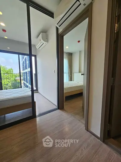 Modern apartment interior with two bedrooms and air conditioning, featuring large windows and wooden flooring.