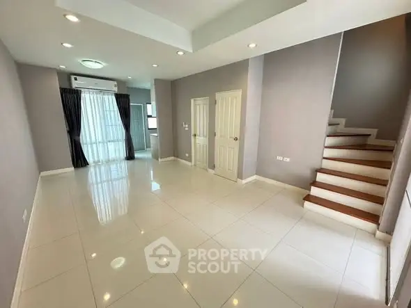 Spacious modern living room with sleek staircase and large windows for natural light.