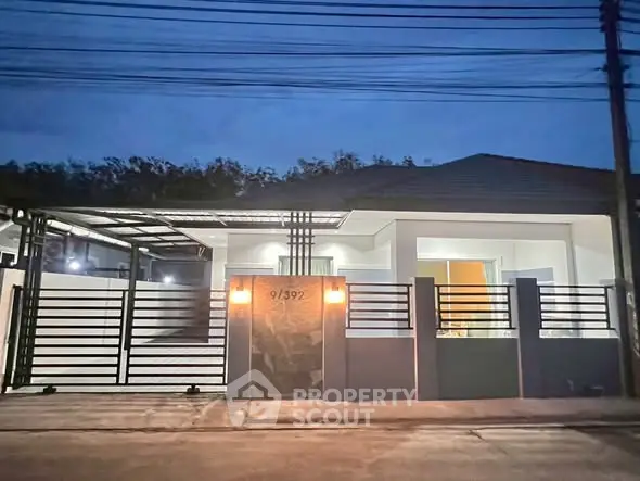 Modern single-story house with sleek fence and warm exterior lighting at dusk.