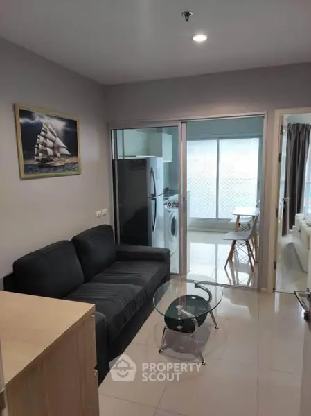 Modern living room with sleek furniture and glass coffee table, adjacent to a bright balcony area.